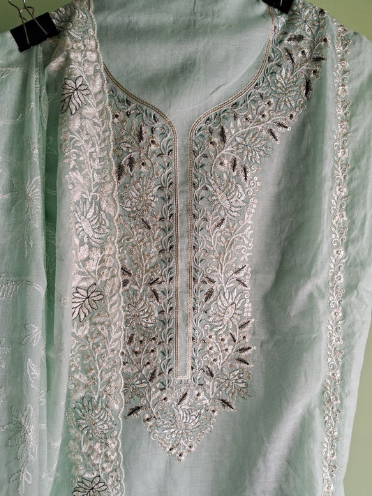 A close-up of a powder blue embroidered tunic top with intricate silver and white floral embroidery around the neckline and lucknowi chikankari dupatta, hanging against a pale green background.