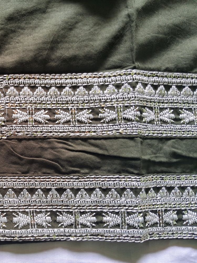 Close-up of a dark olive green mul cotton ready to wear suit set featuring detailed silver and white embroidered borders with geometric and floral patterns.