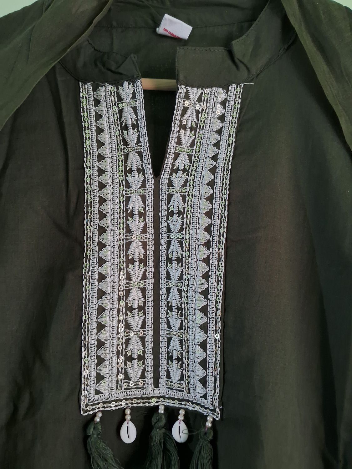 An olive green mul cotton ready to wear suit set embroidered tunic top featuring a wide V-neckline panel adorned with intricate silver and white geometric beadwork and tassels.