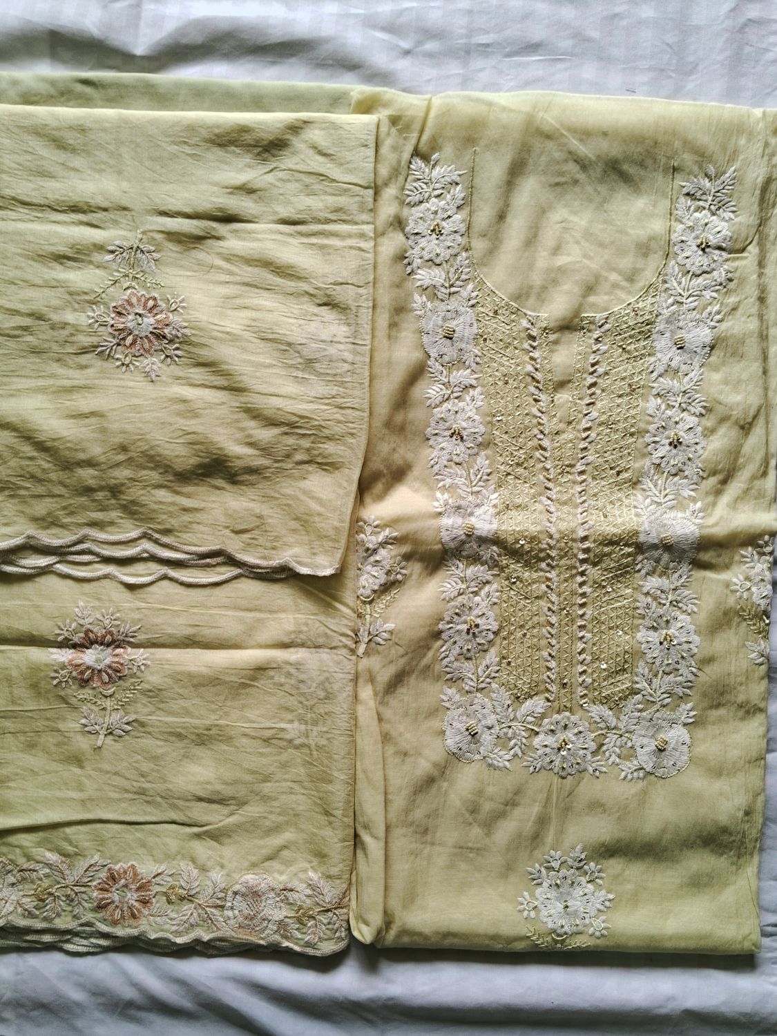 A light lemon yellow- traditional embroidered mul chanderi fabric unstitched dress material laid flat on a white fabric background, featuring white floral embroidery and pink floral accents.