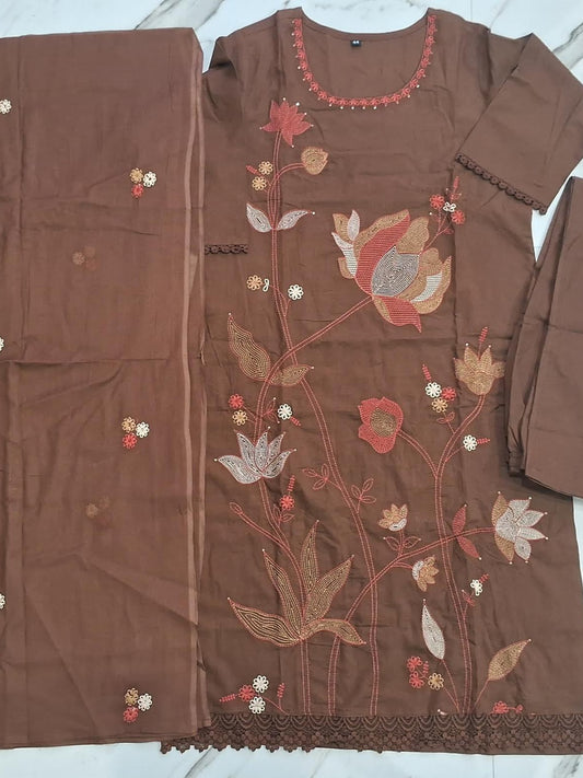 A brown mul cotton 3-piece ready to wear salwar kameez suit set laid flat on a white marble surface, featuring a long-sleeve kurta with floral embroidery, a matching dupatta, and a folded sleeve.
