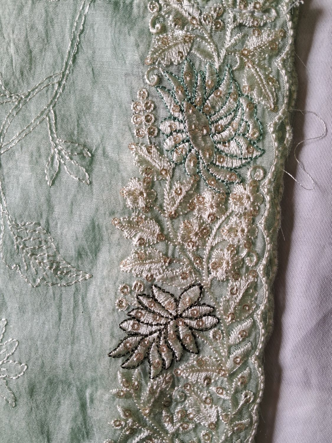Close-up of a light powder blue embroidered lucknowi chikankari dupatta with ornate metallic beige and green floral lace trim.