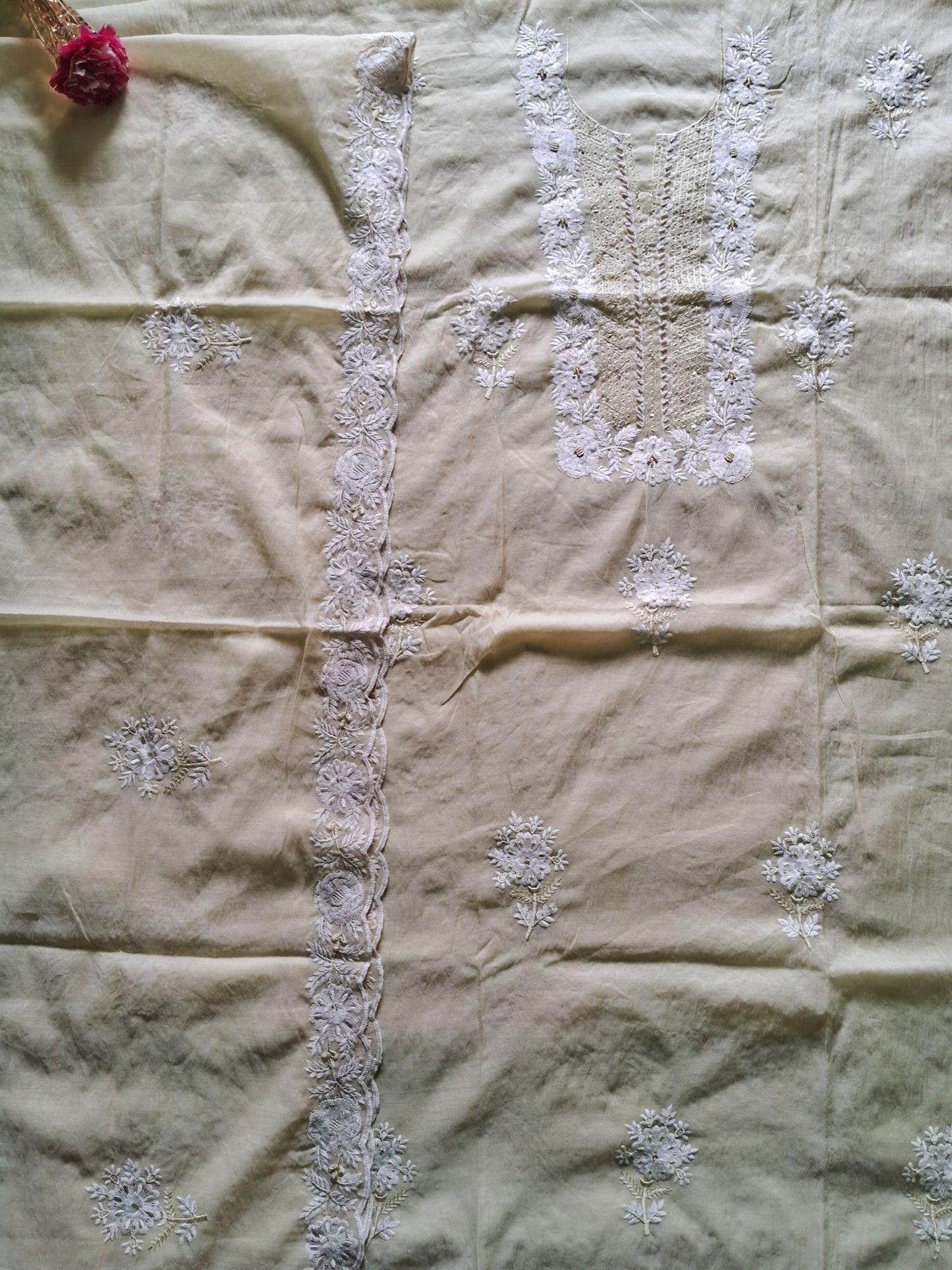 an unstitched dress material lemon yellow mul chanderi fabric with white floral embroidery and border detailing, laid flat with a small pink flower prop in the top-left corner.