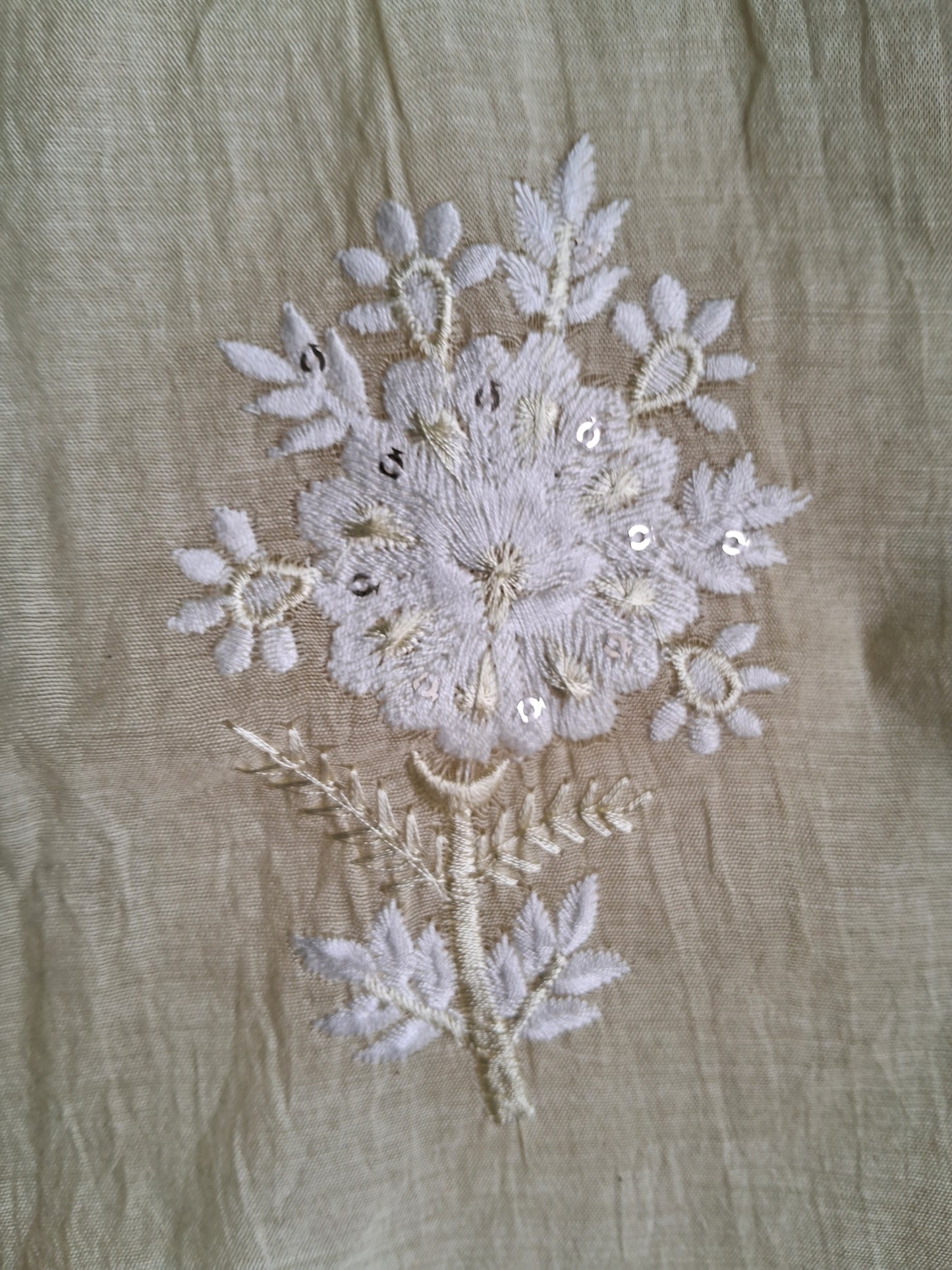 A close-up of a beige mul chanderi fabric featuring a detailed floral embroidery design in white and light gray thread with small silver sequins on a dupatta.